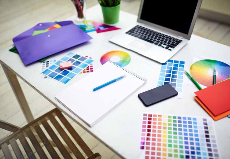 Workplace of designer with color palettes, gadgets, notepad and crayons