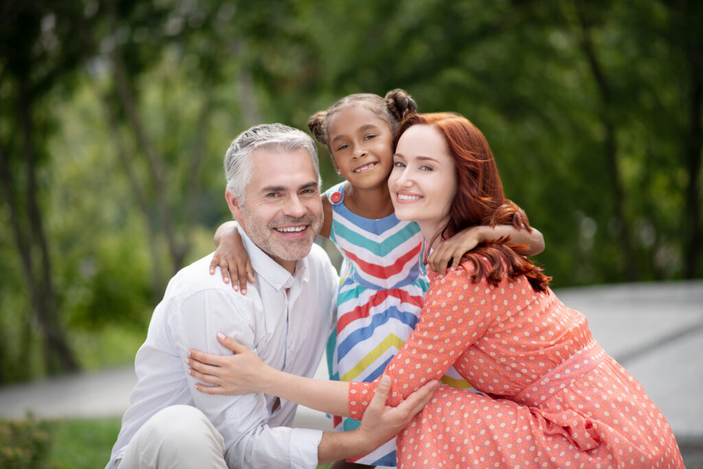 Loving foster parents. Loving foster parents feeling cheerful while hugging their lovely dark-skinned girl