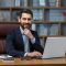Portrait of mature boss inside office with laptop, successful and satisfied investor manager looking at camera and smiling man in glasses and business suit, investor with beard sitting on chair